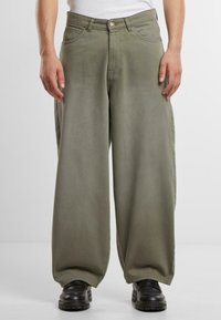 Wide-leg olive green pants made of soft fabric, featuring front pockets, a zip fly, and a relaxed fit, paired with black shoes.