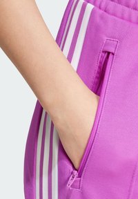 Lila träningshorts med vita ränder, en sidoficka med dragkedja och ett strukturerat tyg för lätt rörelse och komfort.