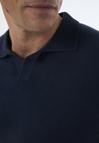 Camisa polo azul marino con un collar texturizado y una tela suave. Primer plano que muestra el escote y los sutiles detalles de costura. Diseño clásico.
