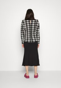 Top de manga longa estampado em preto e branco com decote arredondado, combinado com uma saia preta sólida até o tornozelo e sandálias de plataforma cor-de-rosa.