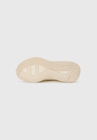 Semelle de sneaker beige clair avec un motif de grip texturé et un logo, présentant une forme arrondie et de subtiles sections compartimentées.