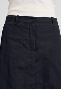 Zwarte hoge taille rok van gladde stof, met een voornaad en metalen knoopsluiting. Eenvoudig ontwerp, zonder zichtbare patronen of accenten.