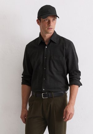 Zwarte geruite overhemd met lange mouwen en knopen, gecombineerd met olijfgroene broek en een zwarte pet. De outfit heeft een klassiek ontwerp en pasvorm.