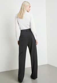 Schwarze, weit geschnittene Hose mit hoher Taille und Gesäßtaschen, kombiniert mit einem enganliegenden weißen Langarmshirt. Glatte Stoffoberfläche.