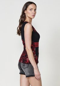 Canotta nera con disegni floreali rossi, senza maniche, silhouette aderente. Abbinata a pantaloni shorts in denim grigio con orli sfrangiati e dettagli in rivetti.