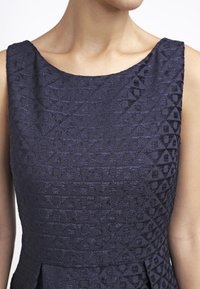 Granatowa, strukturalna sukienka z geometrycznym wzorem, szerokim dekoltem oraz dopasowanym topem z delikatnymi fałdami w talii.