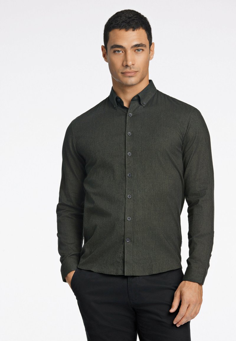 Camisa de botón de manga larga en verde oscuro, con una tela texturizada y botones negros, que presenta un cuello con solapas y un diseño ajustado.