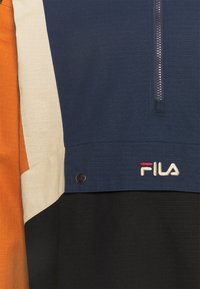 Giacca colorata con pannelli navy, arancione e beige, dotata di zip frontale, tessuto testurizzato e logo ricamato nella parte inferiore.