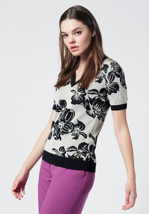 Suéter corto de manga corta con estampado floral en crema y negro, con escote en V, que presenta una forma ajustada y un dobladillo acanalado negro contrastante.