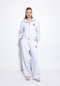 Szara bluza na zamek z kieszeniami, pasujące luźne spodnie dresowe, subtelny detal z logo na piersi, miękka tekstura. Lekki, casualowy design.