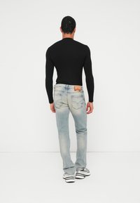 Μαύρο πουκάμισο με μακριά μανίκια, ανοιχτό μπλε ξεθωριασμένο τζιν με πίσω τσέπες. Λευκά και μαύρα αθλητικά παπούτσια. Απλό, λιτό φόντο.