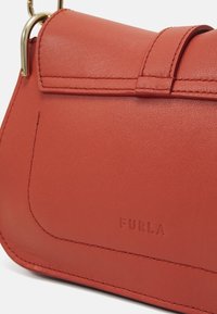 Petit porte-monnaie rouge en cuir avec fermeture à rabat, bords cousus, quincaillerie dorée et logo Furla embossé sur le devant.