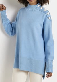 Jersey de canalé azul claro con cuello alto, con aberturas laterales y botones decorativos en el hombro, hecho de un material de punto suave.