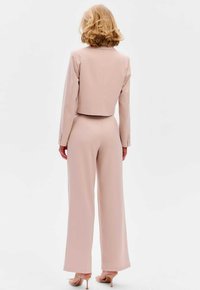 Getailleerde lila blazer met een cropped ontwerp, gecombineerd met wijde broekspijpen. Vloeiend stof met minimale hardware en een gestructureerde silhoutte.