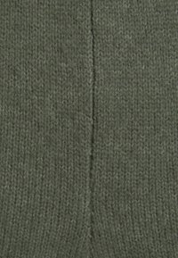 Maslinasto zelena pletena tkanina s mekanom, teksturiranom površinom; ima središnji šav koji ide okomito.