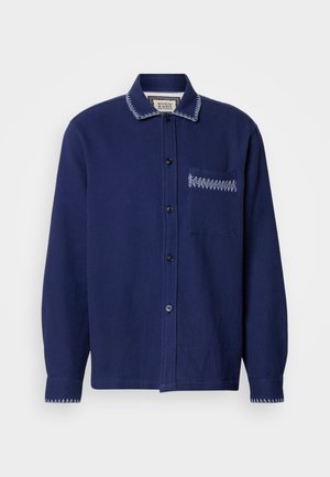 Tengerészkék gombos ing, texturált anyagból készült, gallérral, egy mellzsebbel és kontrasztos varrással a galléron és a zsebben.