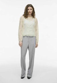 Jasnożółta, przezroczysta bluzka z długim rękawem i teksturowymi akcentami, połączona z szarymi spodniami z wysokim stanem, o dopasowanym kroju i prostych nogawkach.