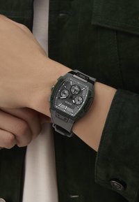 Orologio in quarzo verde e nero con cassa rettangolare, lunetta spessa, tre quadranti secondari, cinturino testurizzato e indicatori delle ore luminescenti.