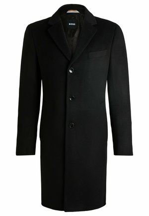 Cappotto lungo in lana nera con risvolto, chiusura a tre bottoni e taschino sul petto. Tessuto liscio, design sartoriale e stile minimalista.