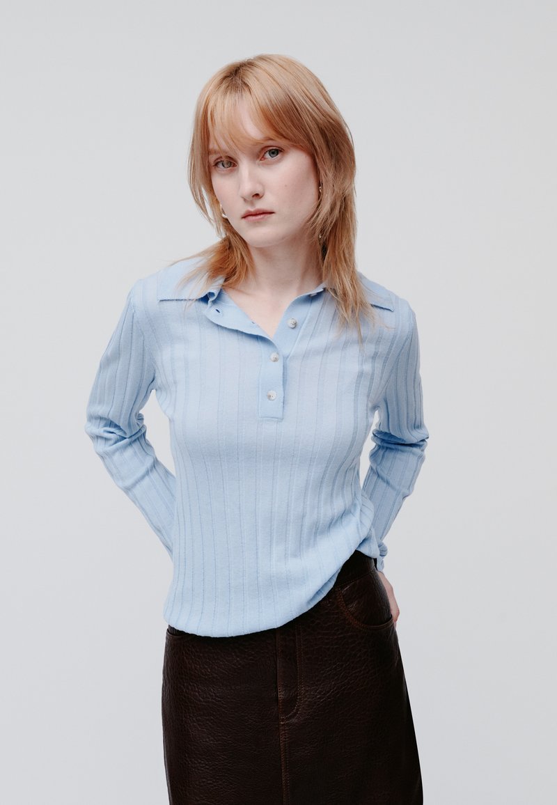 Jasnoniebieska, prążkowana koszula z długim rękawem, z kołnierzykiem i plisą na trzy guziki, zestawiona z ciemnobrązową, teksturowaną skórzaną spódnicą.