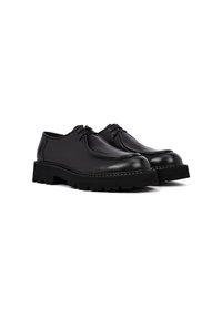 Zapatos de cuero negro con puntera redondeada, detalles de costura y suela de goma con tacos. Presentan un diseño de corte bajo y cierre con cordones.
