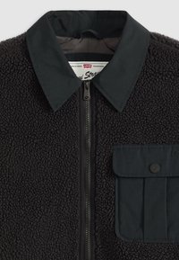 Sort fleecejakke med en kontrasterende krave i sort nylon, frontlynlås og en patchlomme. Tekstureret med en blød, fluffy finish.