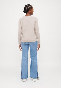 Pull beige à manches longues avec un ourlet côtelé, associé à un jean évasé bleu clair. Le matériau semble doux et texturé.