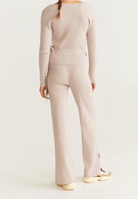 Hellbeige gerippte Strick-Zweiteiler mit einem Taillenknotendetail am Oberteil und weit geschnittenen Hosen, kombiniert mit Sneakers.