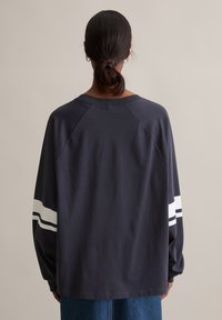 Donkerblauwe longsleeve t-shirt met raglanmouwen, voorzien van witte strepen op de mouwen. Zacht, katoenmateriaal met een ontspannen pasvorm.