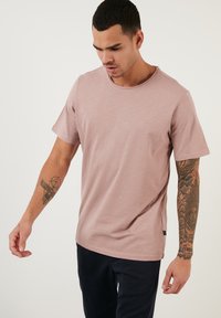 Tricou cu mânecă scurtă și gât rotund, de culoare roz deschis, fabricat dintr-un material moale. Are o croială lejeră și un detaliu discret cu logo pe laterale.