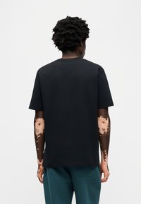 Μαύρο βαμβακερό T-shirt με κλασική γραμμή, κοντά μανίκια και στρογγυλή λαιμόκοψη, με ομαλή υφή και διακριτικές ραφές.