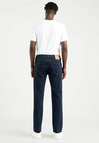 Mörkblå jeans av denim med rak skärning, med en brun läderlapp bakpå och subtil sömnad på bakfickorna, bädda med en vit t-shirt.