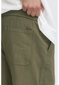 Olivenfarvede shorts lavet af blødt stof med elastisk taljebånd og en enkelt baglomme med rektangulært snit og syninger langs kanten.