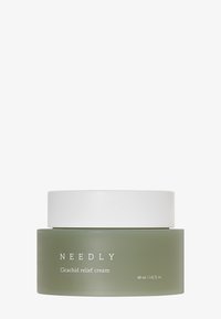 Tarro de vidrio verde con tapa de plástico blanca, etiquetado como "NEEDLY Cicachid crema de alivio", 48 ml / 1.62 oz fl. Acabado suave, diseño minimalista.