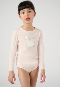 Chemise à manches longues rose clair avec un motif de chat cartoon blanc et le texte "COSY." Le tissu est lisse et la coupe est ajustée au niveau du torse.