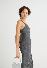 Robe grise scintillante avec un design froncé, des bretelles fines et une silhouette ajustée. Associée à un sac à main à poignée circulaire en argent.