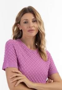 Lilla strikket sweater med tekstureret skællignende mønster, korte ærmer og rund halsudskæring. Glat stof med ribbede detaljer.