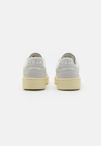 Γκρι και λευκά δερμάτινα sneakers με μαλακή σουέτ φτέρνα, ελαστικές σόλες και έντονη σήμανση "VEJA" στο πίσω μέρος.