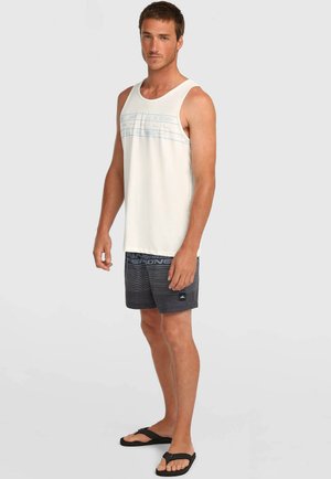 Lichtbeige tanktop met een blauw streepjesontwerp, gecombineerd met donkergrijze zwembroek met horizontale strepen en logo. Zwarte slippers.