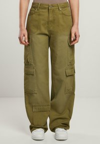 Olivgrüne Cargo-Hosen mit weitem Schnitt, mehreren Taschen und glatter Textur. Mit Knopfverschluss und Gürtelschlaufen, kombiniert mit weißen Sneakern.
