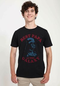Černé bavlněné tričko s textem "NEJLEPŠÍ TAŤKA V GALAXII" červenou barvou, s grafikou postavy v helmě modré barvy. Krátké rukávy, kulatý výstřih.