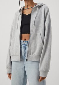 Světlě šedá mikina na zip z měkkého materiálu, s přední kapsou, stahovacími šňůrkami a žebrovanými lemy, spárovaná s džíny s vysokým pasem.