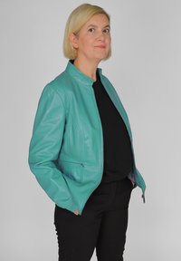 Turqooize leren jas met een rits aan de voorkant, staande kraag en zijzakken. Bevat gestikte details en lange mouwen.