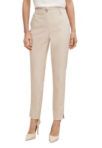 Beige muotipantsit, joissa on sileä pinta, kapea istuvuus, nilkkapituus, sivuhalkiot ja edessä nappikiinnitys. Yhdistettynä kermaisiin korkokenkiin.