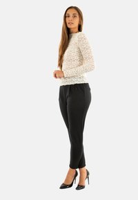 Top in pizzo a maniche lunghe color avorio, abbinato a pantaloni neri su misura con un motivo testurizzato e cordoncino. Tacchi alti neri completano il look.