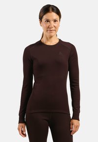 Long-sleeve, fitted thermal top in dark brown, ribbed texture, features a crew neck and subtle branding on the chest. Soft, stretch fabric.