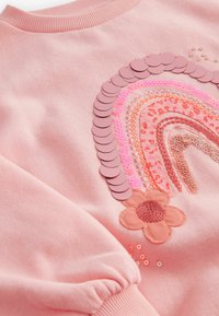 Růžová mikina s duhovým designem, zdobená flitry a vyšíváním. Texturovaný květinový detail na spodním okraji. Hladký výstřih a manžety.
