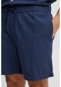Granatowe szorty wykonane z teksturowanej tkaniny, z elastycznym pasem ze sznurkiem, bocznymi kieszeniami i luźnym krojem.