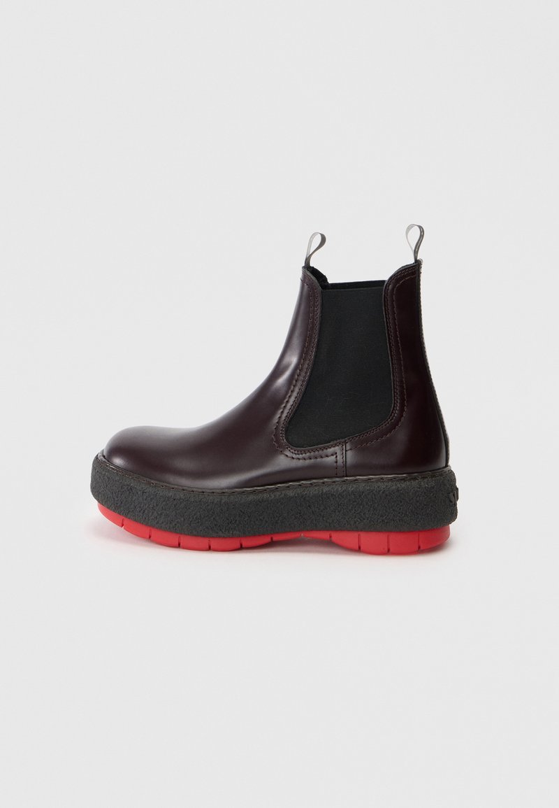 Stivale Chelsea in pelle bordeaux con pannelli laterali elastici neri, suola in gomma con strato rosso sottostante e linguetta sul retro per un facile indossamento.