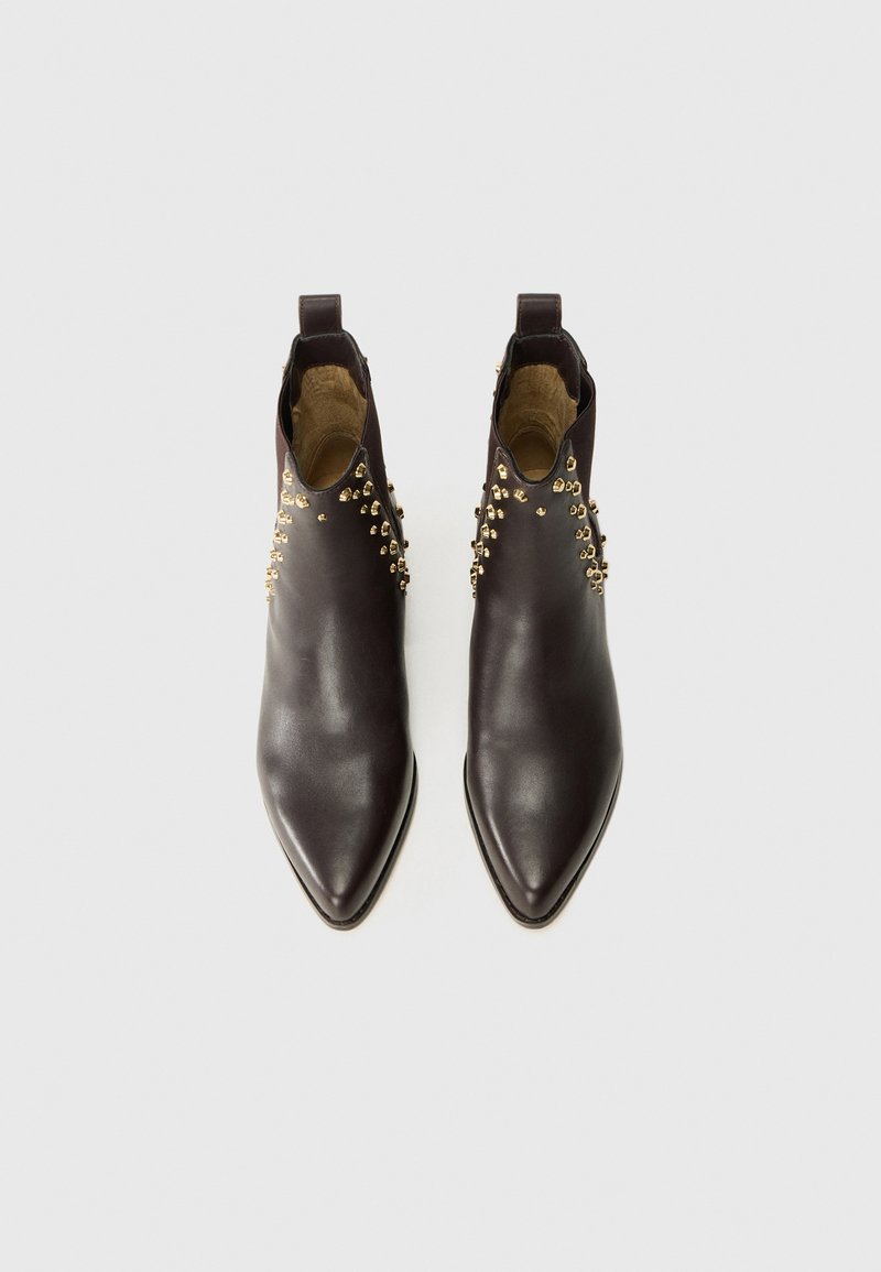 Braune Leder-Ankle-Boots mit spitzer Zehenform, die goldene Nieten an den Seiten haben, aus einer Draufsicht auf einem hellen Hintergrund präsentiert.